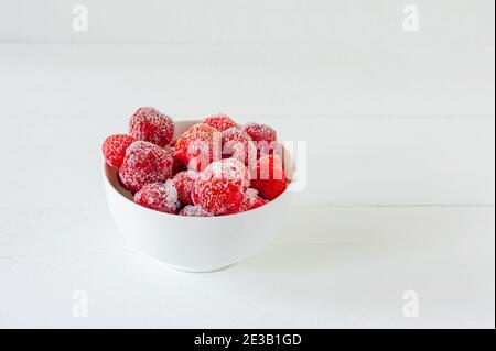 Gefrorene Erdbeere in weißer Schüssel auf einem Holztisch. Beeren mit Reif bedeckt. Stockfoto