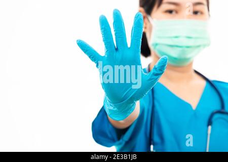 Weibliche Krankenschwester mit Stethoskop setzt Gummihandschuhe und trägt medizinische Gesichtsmaske, Frau Arzt in blauen Uniform zeigen Hand Stop-Zeichen, Studio erschossen isola Stockfoto