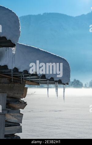 Holzstapel mit verschneiitem Dach und Eiszapfen daran. Holzstapel mit verschneiten Dach und Eiszapfen darauf. Landschaft im Morgenlicht Stockfoto
