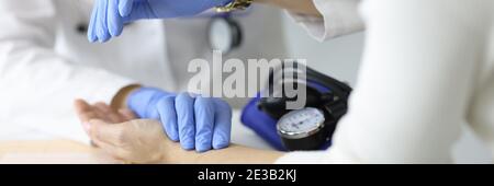 Arzt in Gummihandschuhen Messung Patienten Puls und Blick auf Seine Uhr in der Klinik Nahaufnahme Stockfoto