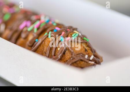 Eine Waffel auf einem Stock, bedeckt mit Schokolade und bunten Süßigkeiten, serviert in einer Papierbox Stockfoto