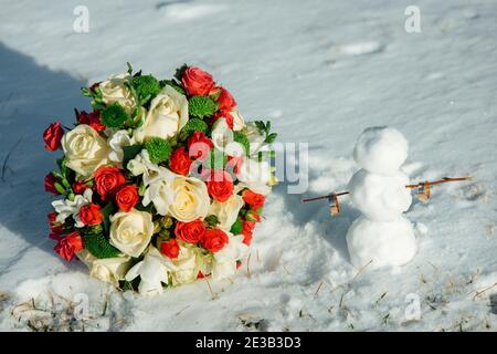 Weiße und rote Rose Brautstrauß im Schnee und Trauringe auf einem Schneemann. Winterhochzeit Stockfoto