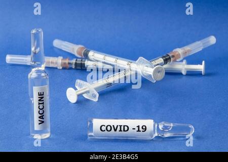 Zwei Fläschchen mit Covid-19-Impfstoff und Spritzen auf blauem Hintergrund. Nahaufnahme Stockfoto