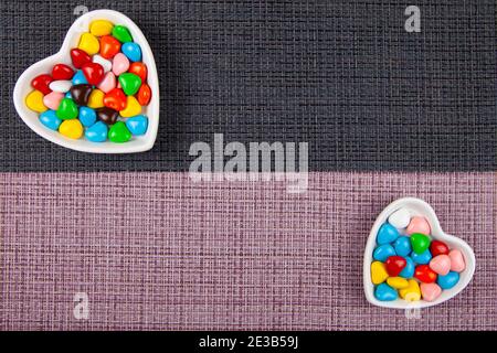 Bunte Bonbons in einem herzförmigen Teller auf schwarzem und pinkem Hintergrund. Valentinstag. Ort für Ihren Text. Stockfoto