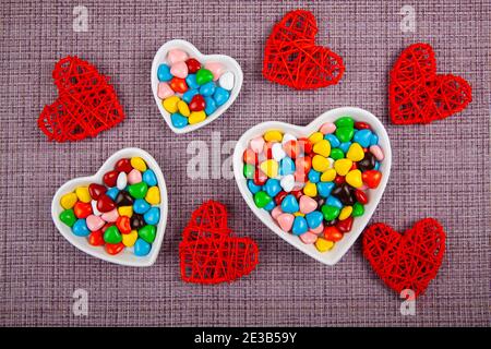 Bunte Bonbons in einem herzförmigen Teller auf einem rosa Hintergrund. Valentinstag. Stockfoto