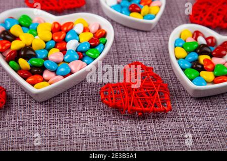 Bunte Bonbons in einem herzförmigen Teller auf einem rosa Hintergrund. Valentinstag. Stockfoto