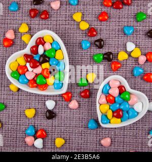 Bunte Bonbons in einem herzförmigen Teller auf einem rosa Hintergrund. Valentinstag. Stockfoto