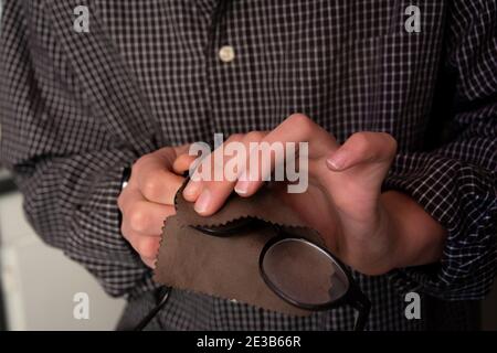 Mann, der seine Brille mit einem Tuch aus nächster Nähe mit selektivem Fokus reinigt. Stockfoto