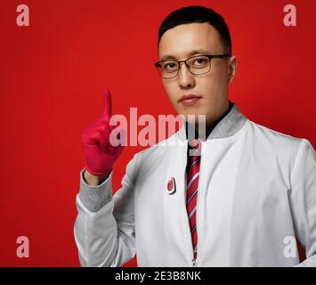 Porträt des jungen Mannes Arzt Urologe oder Proktologe Experte in Uniform Kleid und Latexhandschuhe hält Zeigefinger nach oben Stockfoto