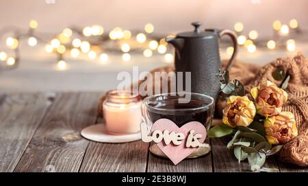 Ein festliches Stillleben zum Valentinstag mit einem Getränk in einer Tasse, Blumen und Dekordetails auf einem verschwommenen Hintergrund mit Bokeh. Stockfoto