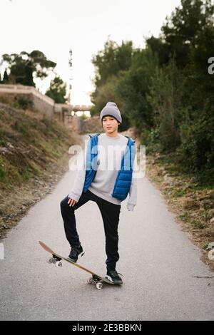 Porträt EINES Teenagerjungen sitzt auf seinem Skateboard in Ein Pfad Stockfoto