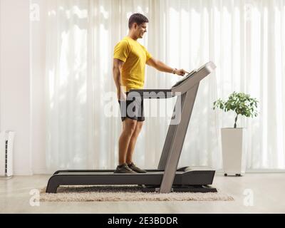 Ganzkörperaufnahme eines jungen Mannes in Sportbekleidung Drücken Sie einen Knopf auf dem Laufband zu Hause Stockfoto