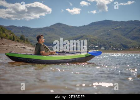 Junger Mann in einem Kanu Angeln auf einem See umgeben In den Bergen Stockfoto