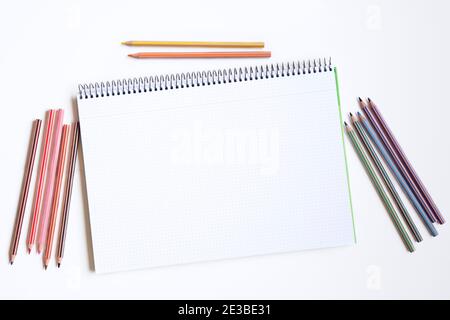 Draufsicht auf ein offenes Notizbuch und mehrere Bleistifte Verschiedene Farben gegen weißen Hintergrund Stockfoto