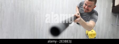 Mann hält den schwarzen Schlauch des gelben Staubsaugers in der Hand und hebt ihn an. Stockfoto