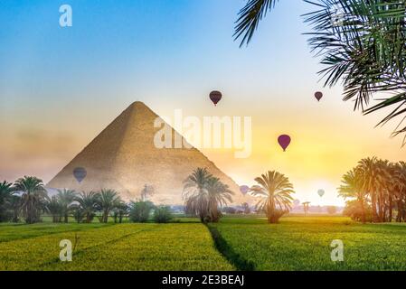 Luftballons über der ägyptischen Pyramide im grünen Feld am nebligen Morgen. Fantasielandschaft mit ägyptischer Pyramide Stockfoto