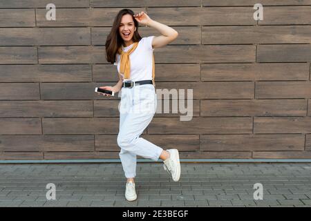 In voller Länge Körpergröße Foto von ziemlich Brunet junge glücklich Frau trägt legere Kleidung und hört Musik über Wireless Ohrhörer, die im stehen Stockfoto