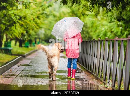 Kleines Mädchen, der Hund unter Regen läuft Stockfoto