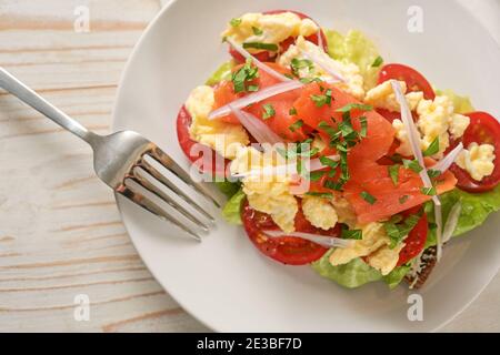 Geräucherter Lachs und Rührei mit Zwiebel und Petersilie garnieren auf ganzer Mahlzeit Brot mit Tomaten und Salat, gesunde Sandwich-Snack auf einem weißen Teller Stockfoto