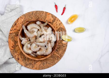 Rohe Garnelen oder Garnelen in Holzplatte mit Limette und rotem Paprika bereit zum Kochen. Eine Schüssel mit frischen rohen weißen pazifischen Garnelen, Zutaten zum Kochen Stockfoto