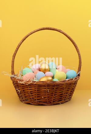 Weidenkorb mit bunten Ostereiern in Pastellfarben auf gelbem Hintergrund. Frohe Ostern Grußkarte Stockfoto