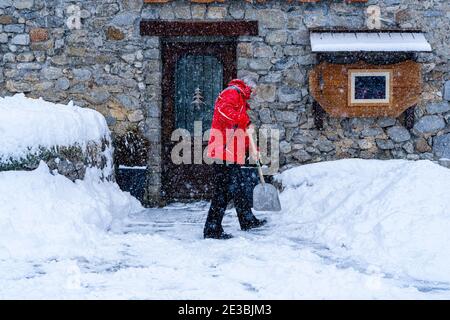 Mann mit Schneeschaufel reinigt Gehwege im Winter in der Nähe des Hauses. Winterzeit, Schneefall. Frankreich Europa. Unscharfer Fokushintergrund Stockfoto