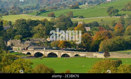 Malerische sonnige Burnsall Dorf (5-gewölbte Steinbrücke, Fluss Wharfe, Hütten, Kirche, Hügel Felder, Herbstbäume) - Yorkshire Dales, England. Stockfoto