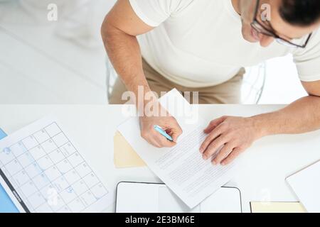 Draufsicht des fokussierten lateinischen Mannes, der mit seinem Laptop arbeitet, Tage im Kalender markiert und Notizen macht, während er auf dem Desktop arbeitet. Online arbeiten, zu Hause studieren Konzept Stockfoto