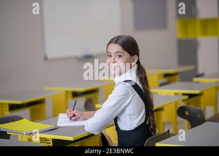 Lächelndes Schulmädchen am Schreibtisch, das ihren Kopf drehte Stockfoto