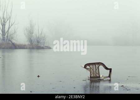 Alt, schmutzig, Kunststoff-Rasenstuhl in gefrorenen See verlassen, neblig und kalten Tag Stockfoto