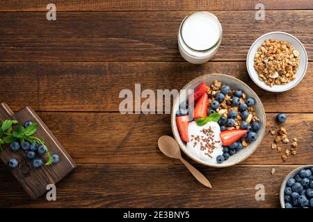 Müslischale mit Beeren und griechischem Joghurt auf rustikalem Holztischhintergrund, Draufsicht Stockfoto