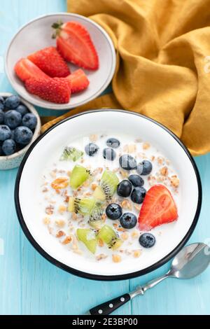 Frühstück Müsli mit Milch und Beeren Heidelbeere Erdbeere Kiwi in Eine Schüssel auf blauem Tisch Stockfoto