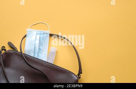 Frauentasche mit Gesichtsmaske und Händedesinfektionsmittel auf gelbem Hintergrund. Konzept für Gesundheit und Sicherheit unterwegs. Stockfoto