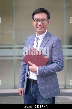 Porträt eines lächelnden asiatischen Geschäftsmannes in Jacke und mit Tagebuch. Stockfoto