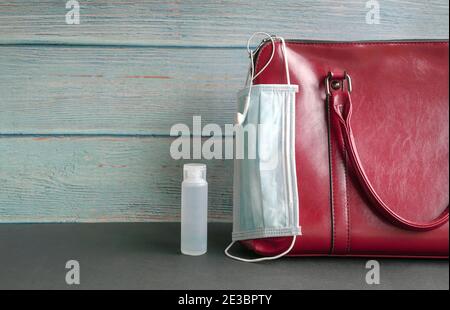 Gesichtsmaske hängt an Frau Handtasche mit Hand Desinfektionsmittel an der Seite. Konzept für Gesundheit und Sicherheit unterwegs. Stockfoto