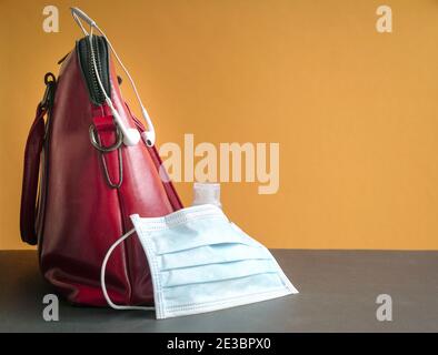 Gesichtsmaske und Handdesinfektionsmittel neben Frau rote Handtasche. Gesundheit und Sicherheit im Freien Konzept. Stockfoto