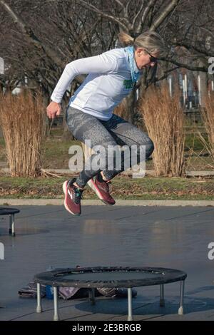 Eine Frau in einer Rebounding-Klasse, die kräftige Bewegungen beim Springen auf einem kleinen Trampolin kombiniert. In Flushing Meadows Corona Park in Queens, NYC. Stockfoto