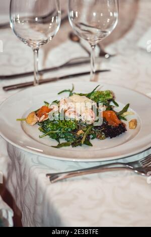Köstlicher Salat mit Lachs und Garnelen in einem Restaurant zum Essen und Wein. Kleine Portion auf einem weißen Teller. Stockfoto