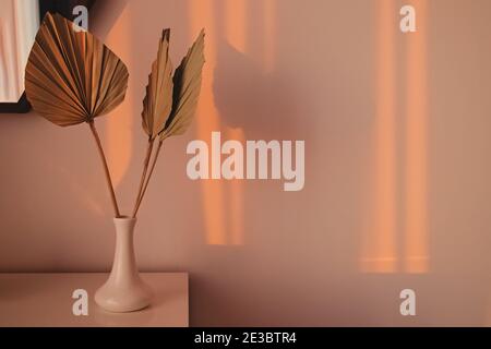 Getrocknete Palmblätter in der Vase und Schatten an der Wand. Stockfoto
