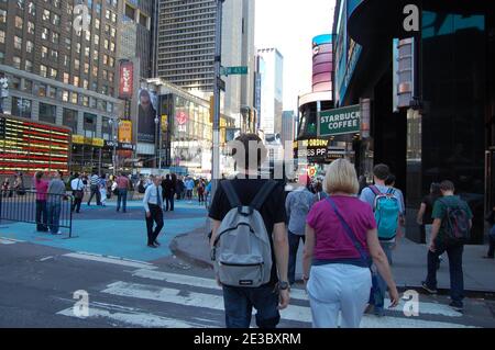 Starbucks Coffee Shop Times Square New York USA Rucksack Walker Touristen USA Flagge Neon leuchtet rot Kappe Teehemd Asphalt gepflasterte Gegend Neon Stockfoto