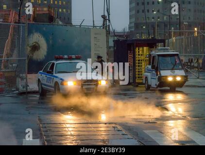 Ein Offizier und ein Polizeifahrzeug mit seinen Scheinwerfern werfen Licht auf Dampf aus den Kanalisation in Lower Manhattan, New York City, USA Stockfoto