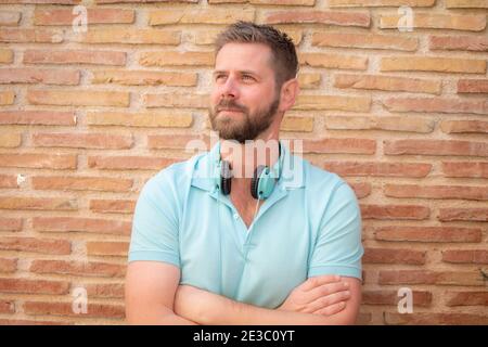 Fröhlicher junger Mann, der Kopfhörer trägt und die Arme im Freien aufgelegt hat Stockfoto