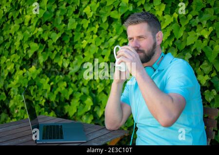 Junger Mann sitzt im Freien mit Laptop-Computer und Kaffee trinken. Stockfoto