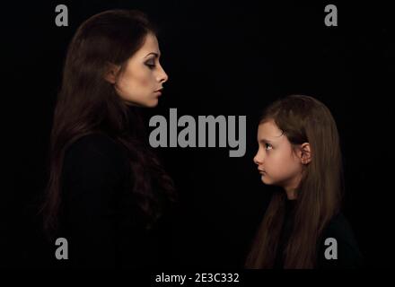 Schöne konzentrierte strenge Mutter und ihre ernsthaft emotional denkende Tochter suchen einander auf schwarzem Schatten Hintergrund. Konzept Familie Emotion Stockfoto