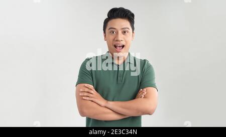 Glücklicher junger Mann. Porträt eines hübschen jungen Mannes, der die Arme gekreuzt und lächelnd vor grauem Hintergrund hält Stockfoto