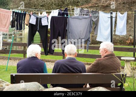 Drei ältere Menschen mit Rücken zur Kamera sitzen auf der Bank Mit Wasch hängend in Reihe im Hintergrund Dunkeld Schottland Stockfoto