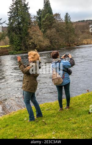 Zwei Frauen, die in entgegengesetzte Richtungen blicken und den Fluss Tay fotografieren Dunkeld Schottland Stockfoto