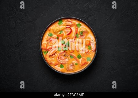 Moqueca mit Fisch und Garnelen in schwarzer Schale auf dunkler Schieferplatte. Brasilianisches Meeresfrüchte-Currygericht mit Kokosmilch und Gemüse. Draufsicht Stockfoto