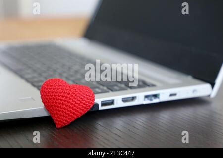 Valentine Heart auf einem Schreibtisch in der Nähe des Laptops. Rot gestricktes Symbol der Liebe, Geschenk für den Urlaub Stockfoto