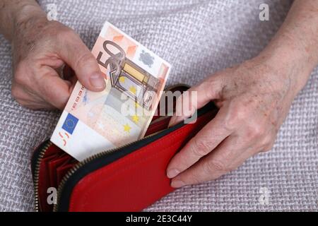 Eine ältere Frau nimmt einen Euro-Schein aus ihrem Portemonnaie. Konzept der Rentenzahlungen, Ersparnisse im Ruhestand, Rentner mit Geld Stockfoto